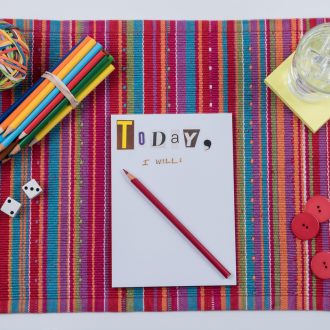 Colorful to do list scene with pad of paper inscribed with, "Today, I Will" - color pencils - red buttons - dices - glass with ice - rubber ball