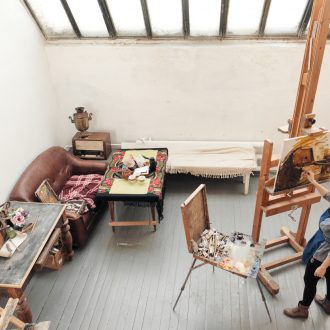 Bright art studio with a large window. Easels and canvases. Woman artist paints a picture on canvas.