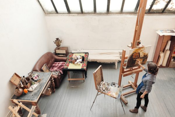 Bright art studio with a large window. Easels and canvases. Woman artist paints a picture on canvas.