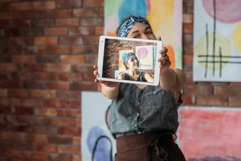 creative-blogger-talented-female-artist-uisng-tablet-to-take-selfie-with-her-artworks-in-studio-blur-background-copy-space