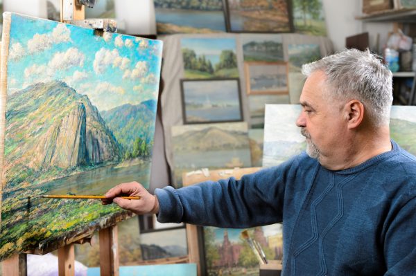 old-man-artist-adding-finishes-touches-to-naturescape-painting-in-art-studio