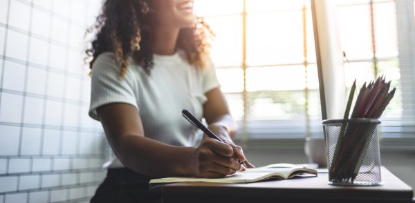 Black woman smiling and writing notes in a journal.