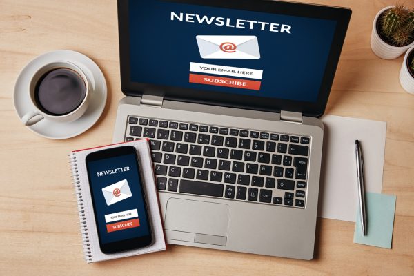 Subscribe newsletter concept on laptop and smartphone screen over wooden table. 