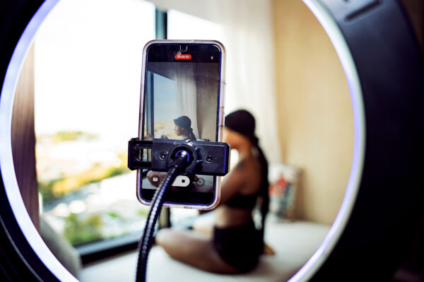 cellphone on stand filming a women in background with bright natural light coming through the window