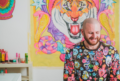 artist in colorful sweater sitting in front of colorful painting