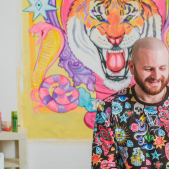 artist in colorful sweater sitting in front of colorful painting