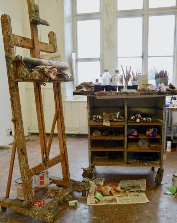 home art studio with paint-splattered heavy-duty easel and supplies on a nearby cart
