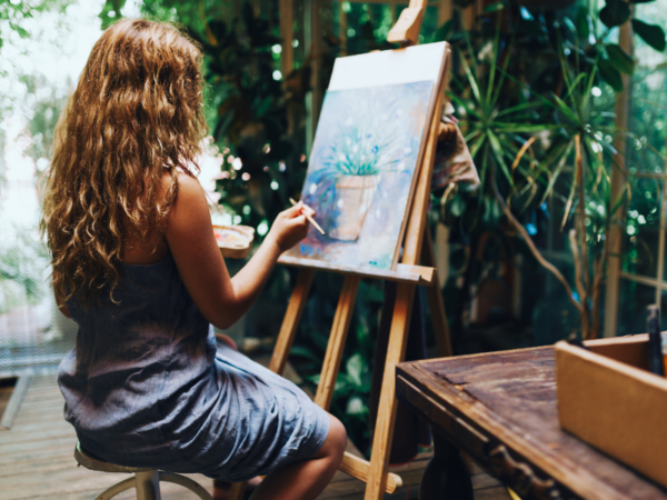 woman painting on easel in a plant-filled studio