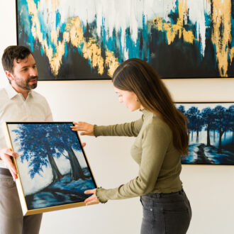 Male artist showing his painting to a female client interested in buying some artwork from the exhibition of the art gallery
